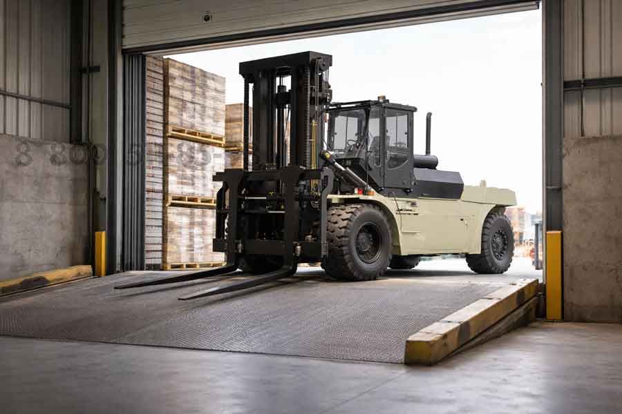 Погрузчик большой грузоподъёмности въезжает через складские ворота по бетонной рампе, вид снизу, акцент на прочную конструкцию и промышленное покрытие.