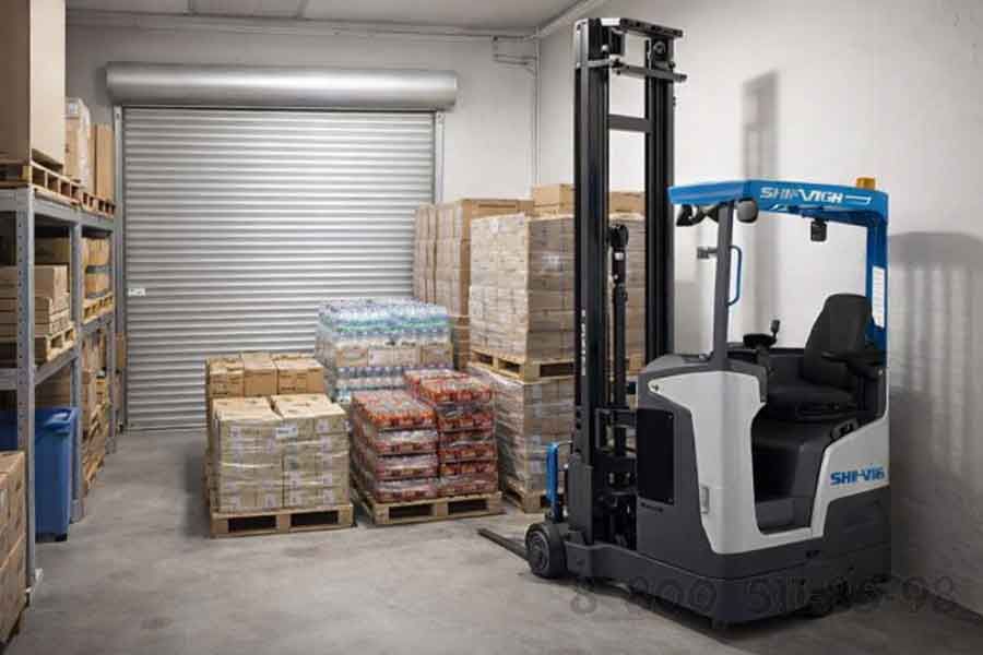 Компактный ричтрак в подсобном помещении супермаркета с паллетами товаров и роллетной дверью, работа в ограниченном складском пространстве магазина