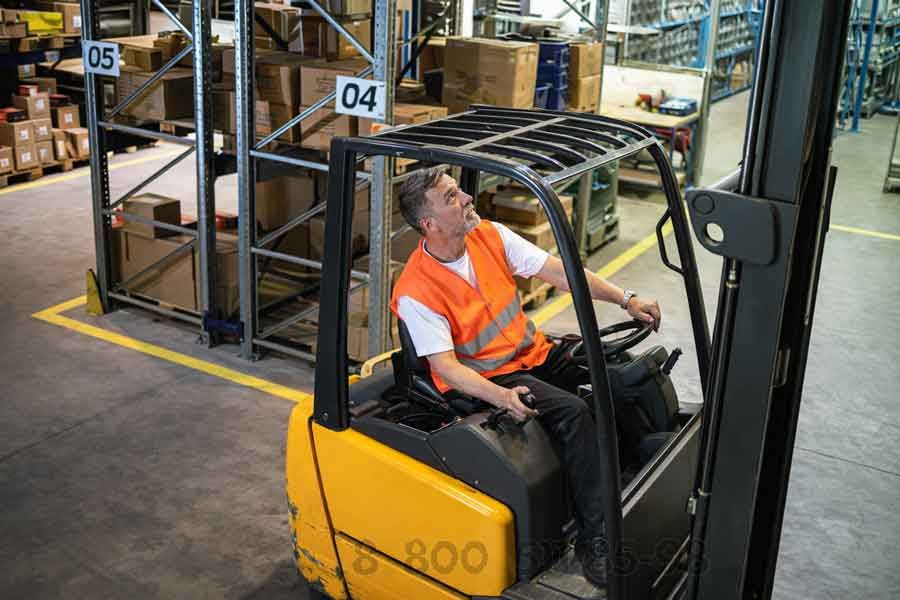 Водитель складского погрузчика управляет техникой в зоне хранения, удобная посадка и контроль мачты при работе на высоте.
