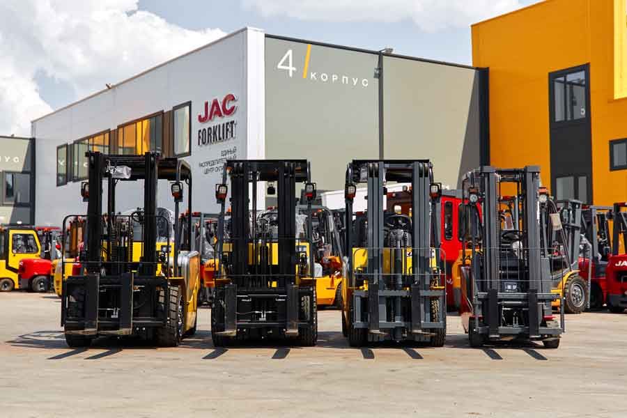 Вилочные погрузчики JAC на открытой площадке перед зданием дилерского центра, складская техника различных моделей и грузоподъёмности.